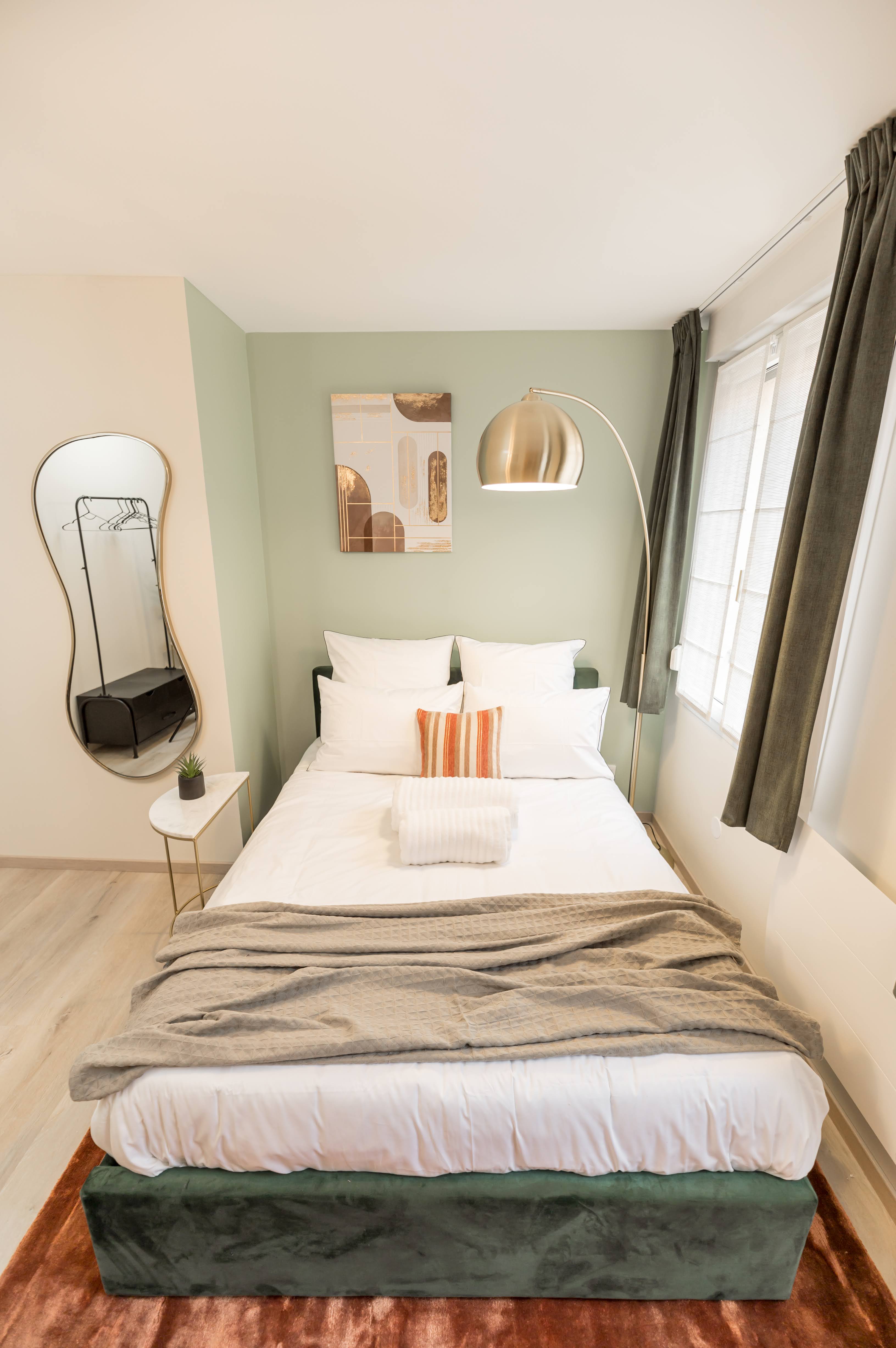 The Secret Garden — petite bedroom with cream and sage green walls, organic mirror and golden arc lamp
